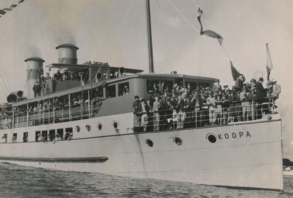 Passengers crowded along the rails of the SS Koopa under flags