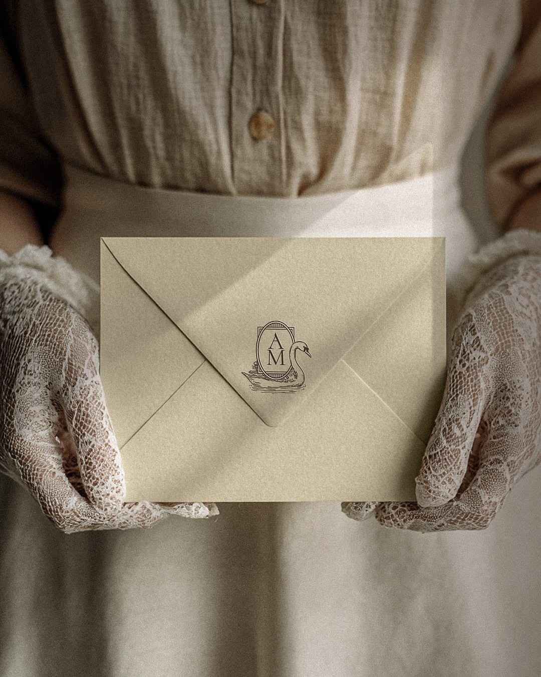 Vintage envelope with monogrammed swan-and-crest engraving held in lace gloves